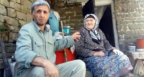 Ramazan Djalaldinov sit near the elderly resident of Kenkhi village. Photo: screenshot of the video appeal.  