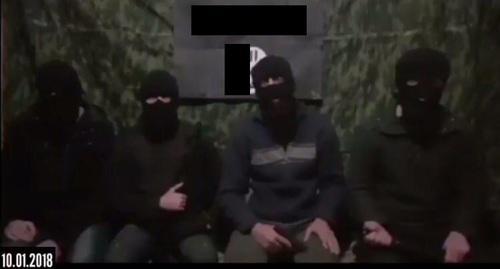 Four masked men sitting at the background of the IS'* flag call on their followers to kill Russian rights defenders. Screenshot of the video.