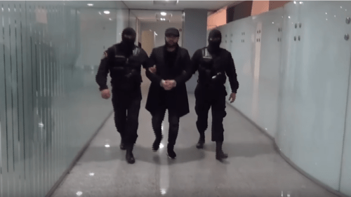 Two masked law enforcers are escorting handcuffed Narek Sargsyan at Zvartnots Airport in Yerevan. Screenshot from video posted at: https://www.youtube.com/watch?time_continue=16&v=1MUWqxKFicE&feature=emb_title