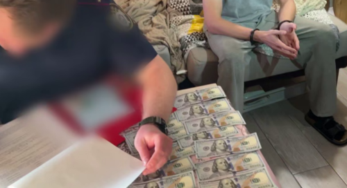 A security officer writes a report on spread out dollar bills. Still from the video of the Investigative Committee of Russia for the Krasnodar Territory from September 25, 2025, https://t.me/kubansledcom/6066